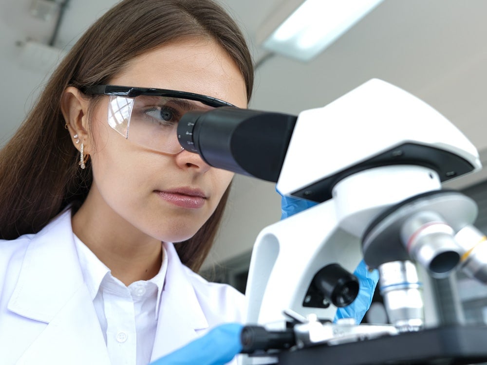 Georgia Southern student, wearing goggles, studying something through a microscope.