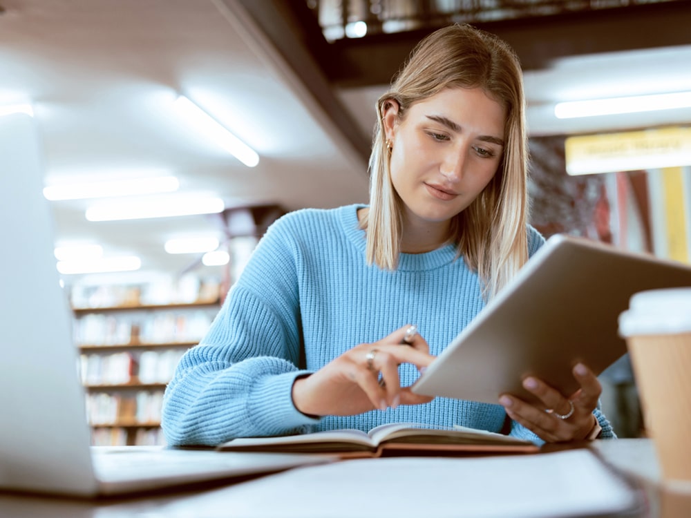 Using a tablet and book, a student from Georgia Southern's M.A. in Professional Communication and Leadership program works on their Comprehensive Project in a campus library