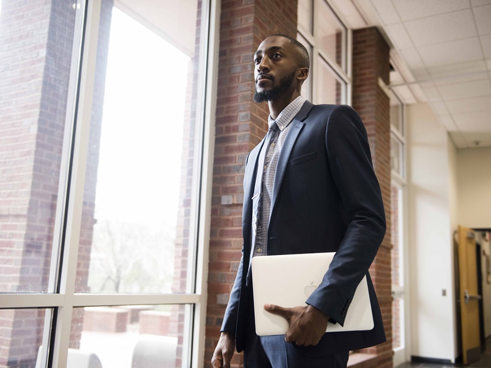 A student from Georgia Southern's M.A. in Professional Communication and Leadership program wearing a suit and holding a laptop heads off to an internship assignment