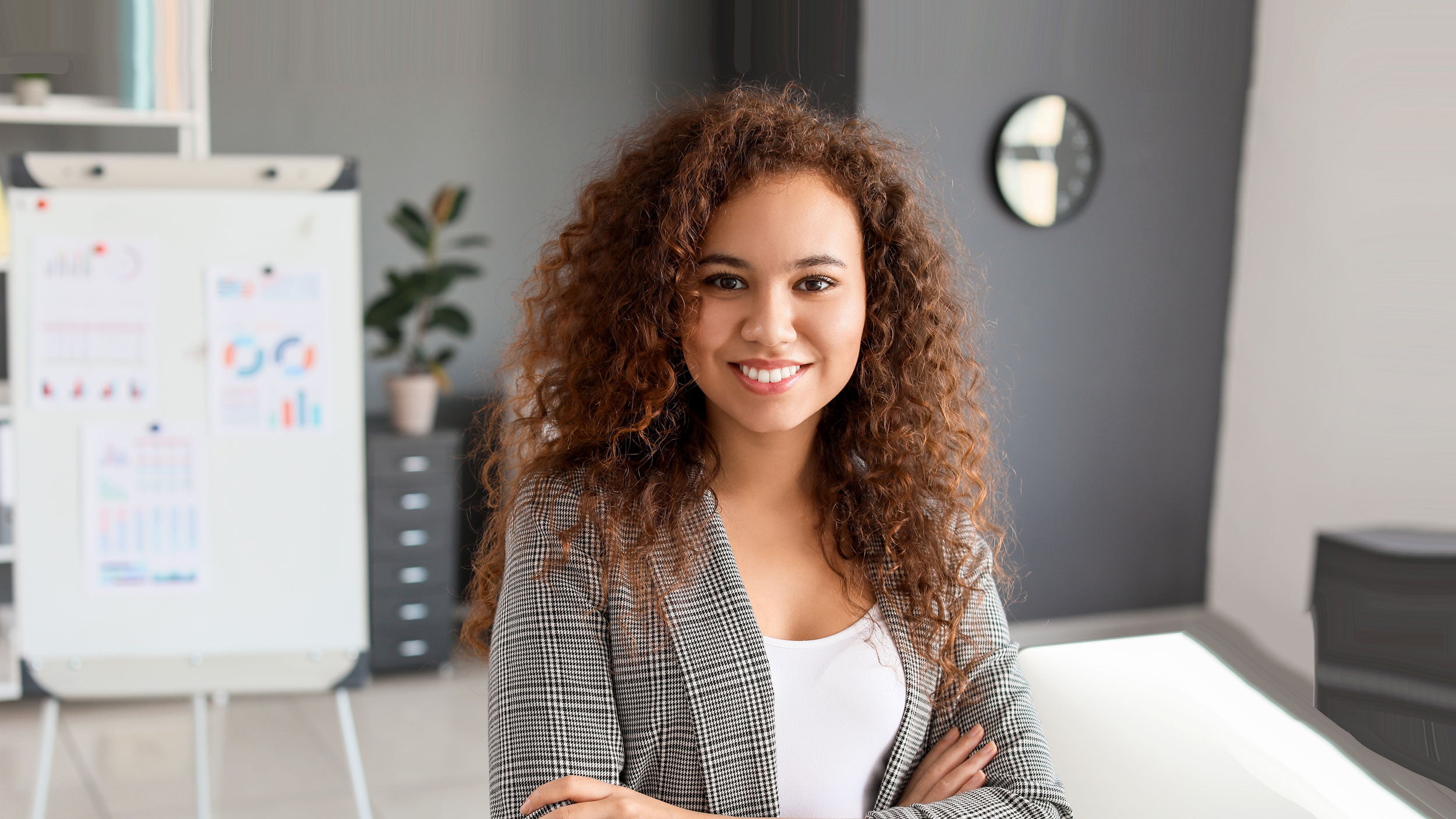 Young woman standing in business office with sales charts behind her.