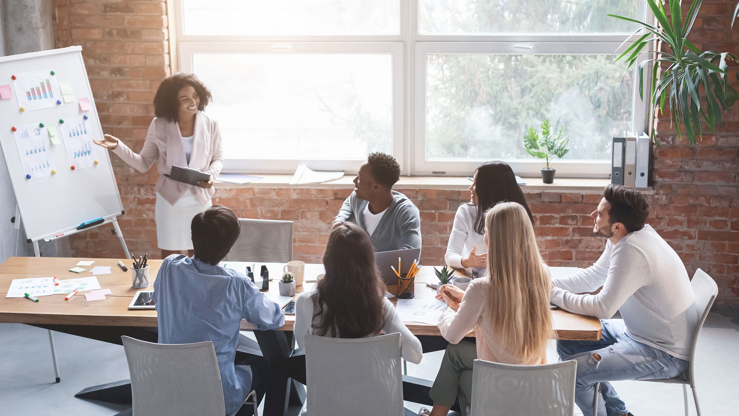 Young woman giving a business presentation to a small group around a conference table.