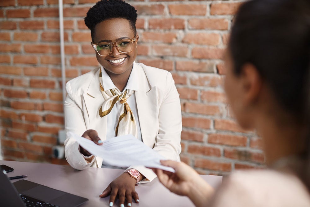 Black female human resource manager handing a document to a student.